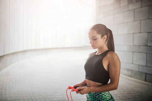 Geweldig en mooie jonge vrouw neerkijkt. Ze staat in grijze gang en houdt oranje ope met beide handen. Model is geconcentreerd. — Stockfoto