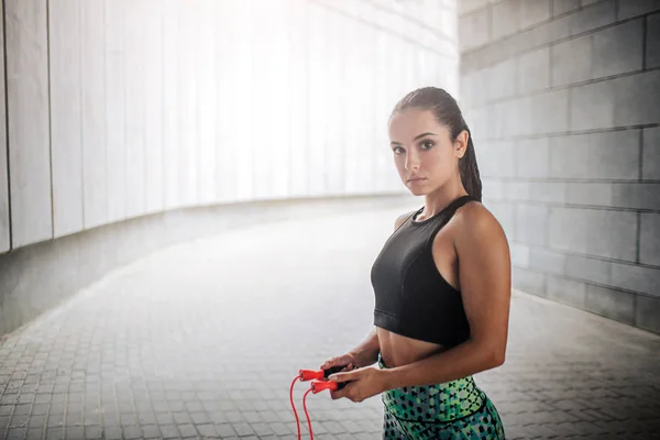 Ernstig en kalm model kijkt op camera. Goedgebouwde model bezit oranje touw met beide handen. Ze is mooi en fascinerende jonge vrouw. — Stockfoto