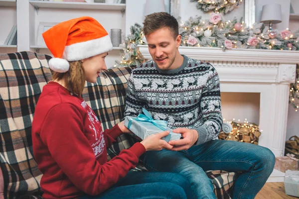 Bild eines jungen Mannes auf dem Sofa sitzend. Er schenkt der jungen Frau eine gepackte blaue Schachtel. Sie ist aufgeregt und glücklich. Der Mensch ist glücklich. sie halten Geschenk zusammen. — Stockfoto