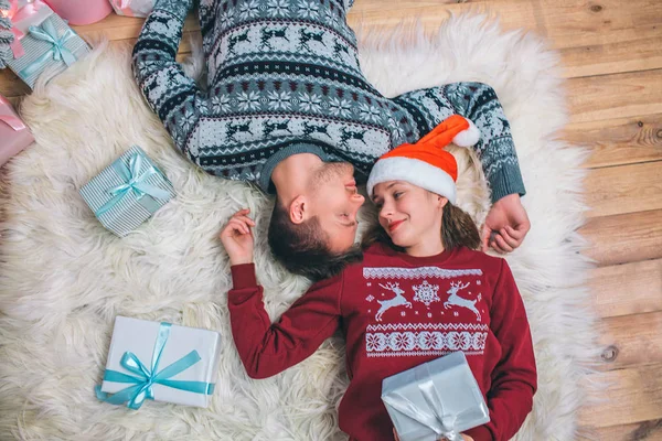 Bonita imagen de pareja feliz acostada en el suelo desde diferentes lados. Se miran unos a otros. La gente sonríe. Tiene un regalo azul en su cuerpo. . — Foto de Stock