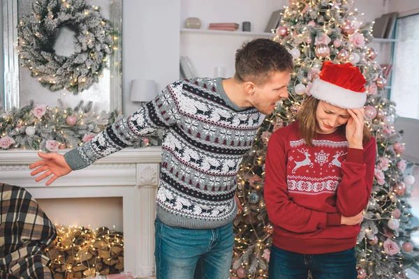 Ein wütender junger Mann steht neben der Frau und schreit sie an. zeigt er nach links. Modell ist verärgert. weint sie. Sie tragen Weihnachtskleidung. — Stockfoto