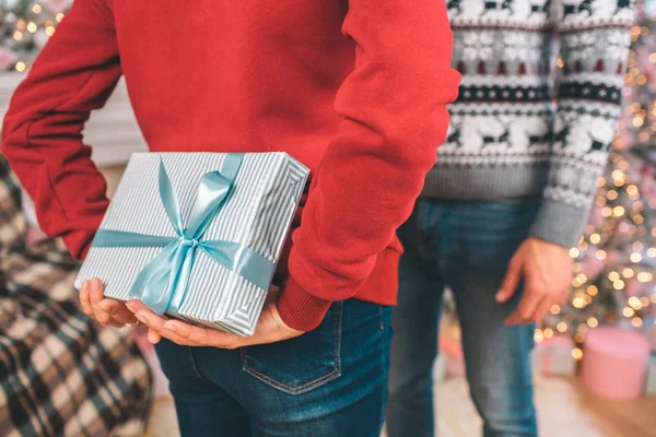 Bild von zwei Menschen, die sich gegenüberstehen. Mensch im roten Pullover hält Schachtel mit Geschenk hinter sich. Menschen verstecken es. — Stockfoto