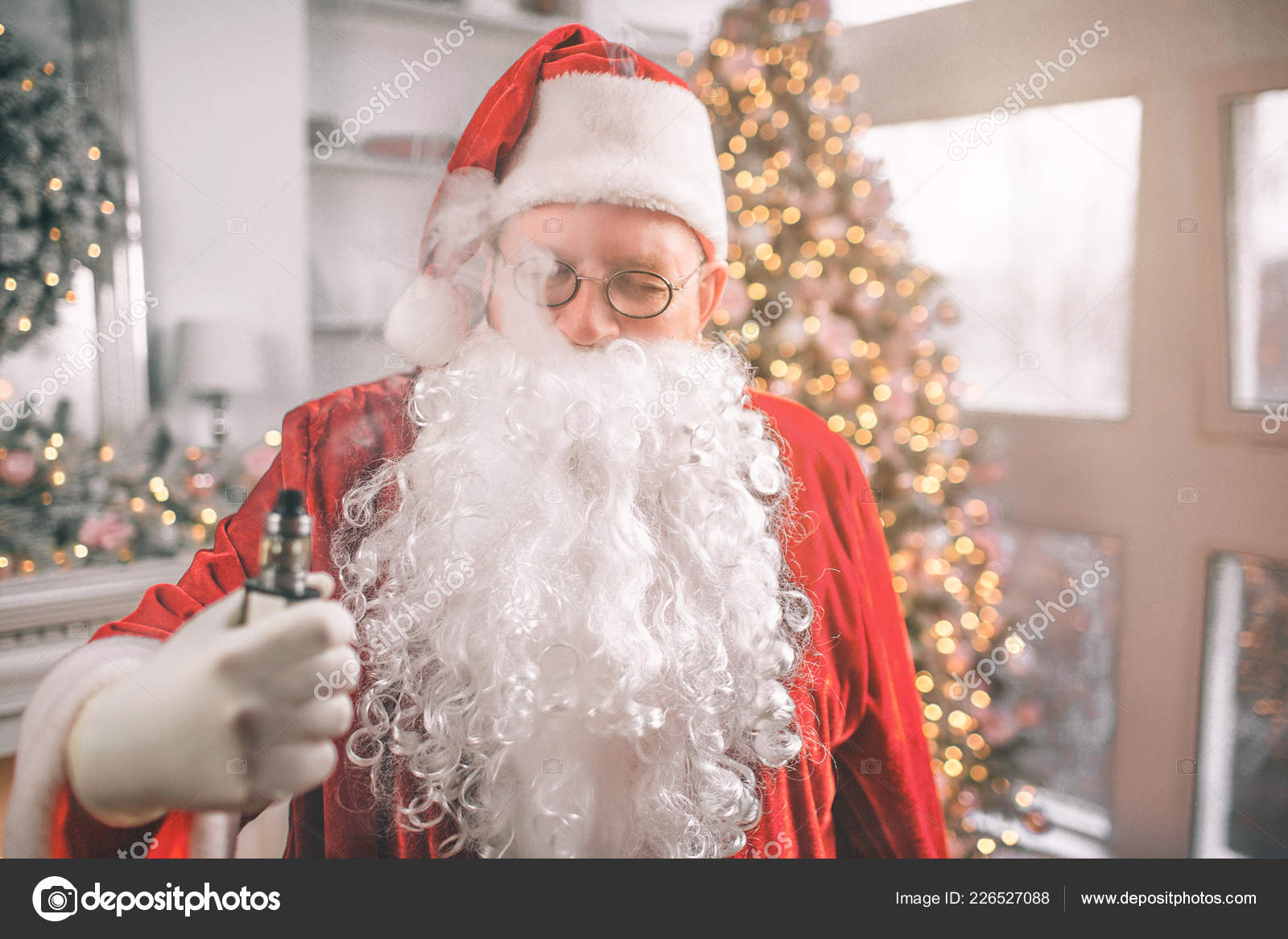 Entspannter Mann im Weihnachtsmann-Kostüm steht und hält Vapiano in der  Hand. Rauch dringt aus seinem Mund. Er ist entspannt. - Stockfotografie:  lizenzfreie Fotos © Estradaanton 226527088