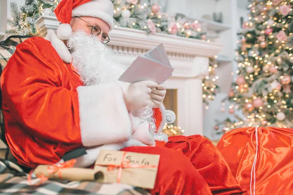 Image du Père Noël assis et lisant des lettres. Il les tient dans ses mains. L'homme est concentré et sérieux . — Photo