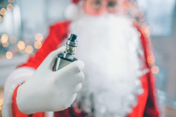 Gros plan du Père Noël se tient debout et tient vape dans la main. Il le montre à la caméra. . — Photo