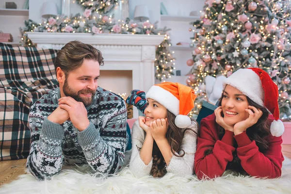 Positive junge Frau und Mädchen, die auf dem Boden liegen und den Mann betrachten. Sie halten die Hände unter dem Kinn. Der junge Mann tut dasselbe. er lächelt Mädchen an. — Stockfoto