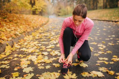 Genç kadın jogger kadrosu konumu ve kravat dantel ayakkabıları üzerinde oturur. O kulaklık üzerinden müzik dinlemek. Genç kadın konsantre.