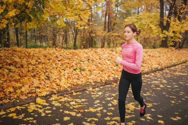 Kobiece jogger działa na drogi w parku. Ona jest sam. Model kształcenia. Jest jesień, poza. — Zdjęcie stockowe