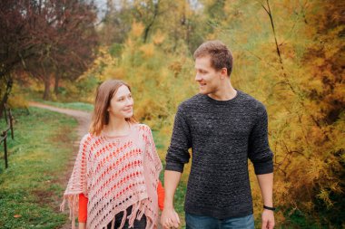 İki genç duran ve birbirlerine el ele tutuşarak insanlar. Bak ve gülümse. Yürürler. Genç adam ve kadın parkta vardır.