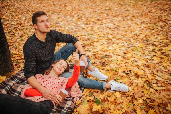 Hermosa pareja sentada y acostada en el parque de otoño sola. Miran en la misma dirección. Mujer acostada sobre piernas de chicos. El tipo se sienta en la manta. Tienen una taza de café. . — Foto de Stock