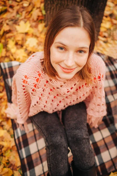 Retrato de una joven sentada sola en el parque. Es otoño afuera. Ella mira a la cámara y sonríe . — Foto de Stock