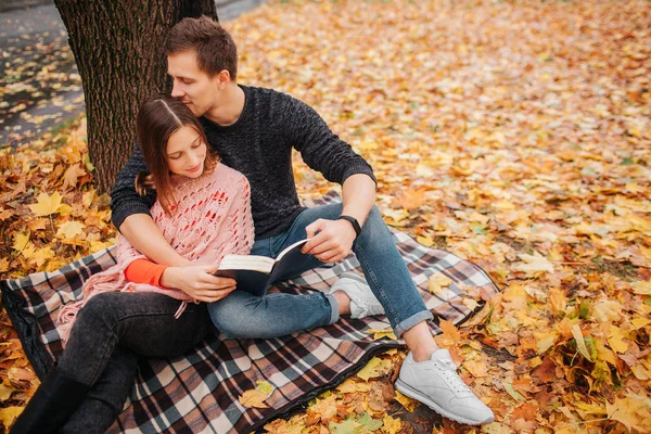 Foto de Lovelu de un joven sentado sobre una manta con una mujer. La abrazó y la besó. Ella mira el libro. Lo mantienen unido. . — Foto de Stock
