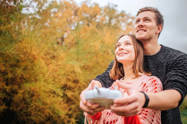 Happy and cheerful young man and woman look up. They hold remote control together. People stand in autumn park. — Stock Photo, Image