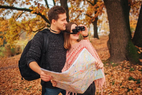 Hombre guapo está junto a la mujer y sostiene los prismáticos. Ella mira en ella. Mantienen el mapa unido. La gente está en el parque . — Foto de Stock