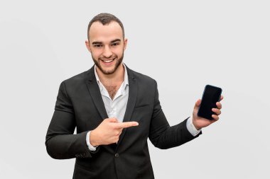 Telefon mutlu işadamı puan. O elinde tutar. Kamera ve gülümseme bak genç adam. Beyaz arka plan üzerinde izole.