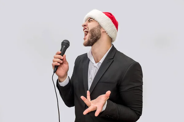 Adult singer singing song in microphone. He screams and moves with hand. Young man wears suit and Christmas hat. Isolated on white background. — Stock Photo, Image