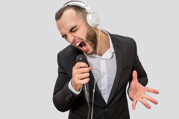 Imagen de un joven de traje gritando con un micrófono. Canta la canción. El tipo se encoge y se mueve con la mano. Aislado sobre fondo blanco . —  Fotos de Stock