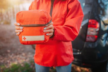 Picture of orange firt aid kit bag young oman hold with both hands. She stads at tent. Model wears orange jacket. clipart
