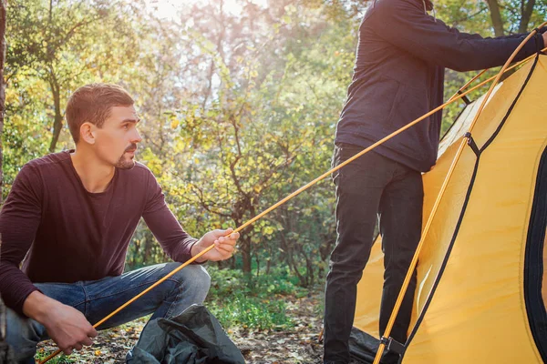 Cut view of two men working. First holds rope while another touches tent. They are in forest.