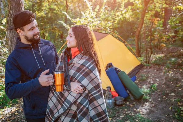 Preciosa imagen de pareja joven de pie en la tienda y mirándose. Está cubierta de manta. El tipo tiene termotaza. La gente está tranquila y feliz. . — Foto de Stock