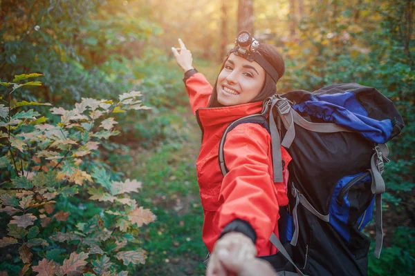 Живопись веселой молодой женщины, путешествующей по лесу. Она носит рюкзак на спине. Молодая женщина держит камеру и указывает вперед. Она улыбается. . — стоковое фото