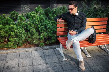 Ciddi genç adam o tutan telefon görünüyor. Adam bankta oturmak. Başka bir bacağı vardı. Onu yanında siyah deri çanta vardır.