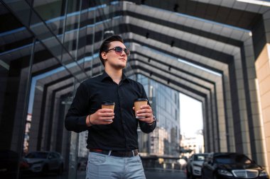 Ciddi ve yoğun genç adam kameraya poz. Düz görünüyor. Adamın iki kağıt bardak içki var. Ark durduğunu.