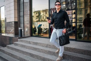 Genç işadamı kameraya poz. Merdiven üstünde yürüyor. Adam telefon ve siyah çanta tutar. Genç adam dışarıda.