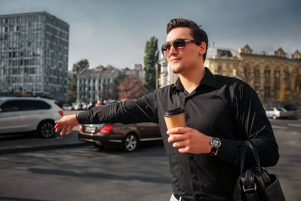 Le jeune homme se tient dehors et tient une tasse de boisson. Il tient la main. Guy essayer de prendre un taxi . — Photo