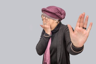 Korkmuş ve genç Arap kadın coveres yüzünü korkuttu. Kamerada avucunun gösterir. Gri arka plan üzerinde izole.