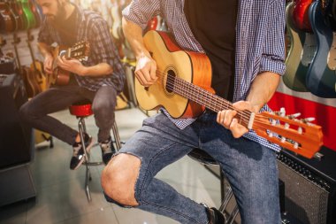 İki müzisyen küçük akustik gitar çalmaya. Onlar özel dinlersem. Onların arkasında birçok elektro gitar vardır.