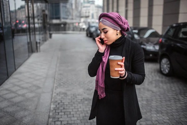 Elfoglalt, és komoly fiatal Arab nő kívül és lenézni. Ő beszél a telefon és a hold csésze, ital. — Stock Fotó