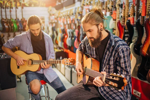 두 젊은 남자 어쿠스틱 기타에 집중. 그들은 전기 기타에 전체 방에 발판에 앉아. 수염된 들 함께 플레이. — 스톡 사진