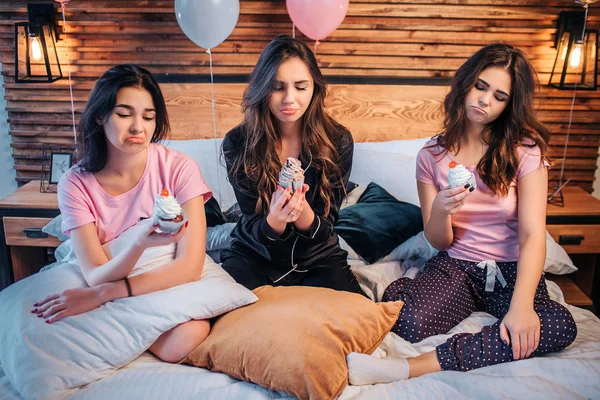 Ledsen och upprörd unga kvinnor sitta på sängen i rummet. De håller kakor och titta på dem. Unga kvinnor är missnöjda. — Stockfoto
