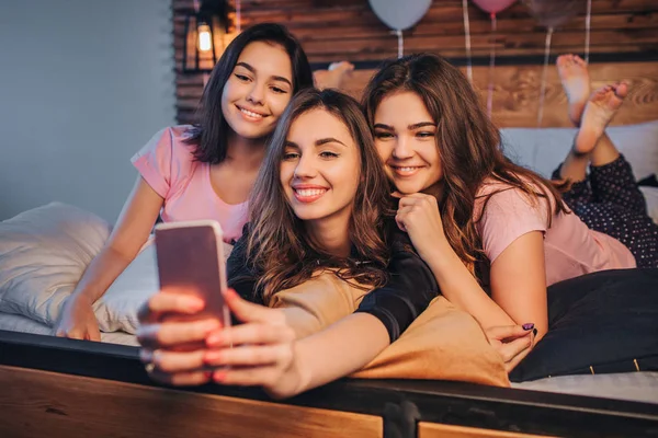 Drei junge Models beim Selfie. Sie posieren und lächeln. Gils sind im Zimmer. Einer von ihnen hält sein Handy in der Hand und fotografiert es. Junge Frauen sind fröhlich. — Stockfoto
