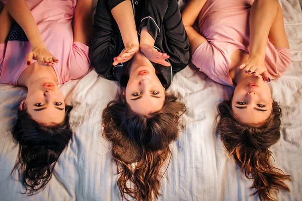 Três modelos adoráveis de oyung deitado na cama e olhando para a câmera. Mandam-lhe beijos. As raparigas usam pijama. Isaolted no fundo branco . — Fotografia de Stock