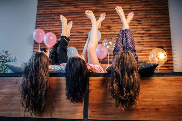 Drei junge Frauen mit wunderschönen und schönen Haaren, die auf dem Bett im Zimmer liegen. sie halten die Beine hoch. Models posieren. — Stockfoto