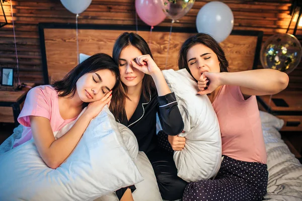 Schläfrige junge Models sitzen zusammen auf dem Bett in einem festlichen Raum. Sie wollen schlafen. einer von ihnen schläft schon. — Stockfoto