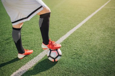 Vücut futbolcu alt kısmı resmi. O yeşil sahada ayakta ve tek ayak üzerinde topu tutun. Beyaz hattı yeşil çim gelir.