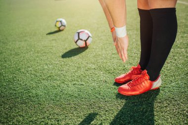 Futbol oyuncu kürsüye çim ve yeşil alan aşağı germe. Bacaklarını tutar ve birlikte eller. Daha fazla yalan iki futbol topları.