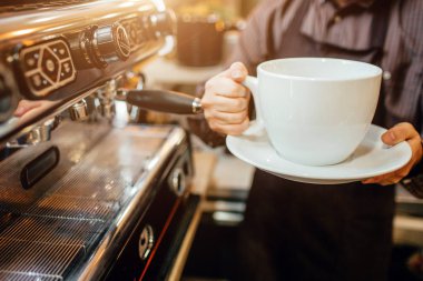 Büyük beyaz fincan kahve elinde tutan barista görünümünü kesti. O kahve makinesi, mutfak duruyor.
