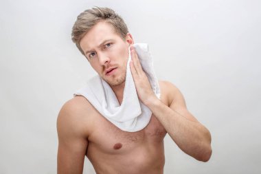 Endişeli genç yakışıklı adam yanak beyaz havlu ile silin ve kameraya bak. O yoğun ve üstsüz. Beyaz arka plan üzerinde izole.