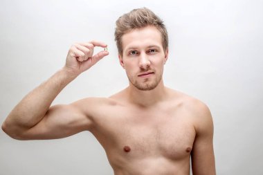 Çekici bir genç adam düz bak. O iki parmak arasında altın yüzük tutun. Beyaz arka plan üzerinde izole.