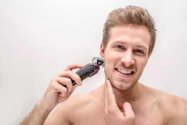 Tıraş makinesi ile neşeli genç adam. O gülümser ve çene dokunur. Beyaz packground izole.