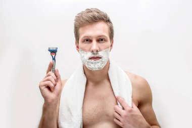 Köpük sakal üzerinde ciddi genç adamla razers elinde tutmak ve kameraya göster. Hiç birine düz ön. Beyaz arka plan üzerinde izole.