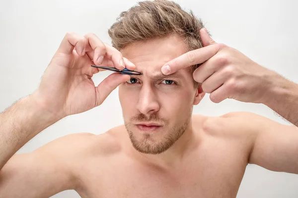 Bild av ung blond man gungade ögonbryn. Han ser raka. Kille hålla pincett i hand. Isolerad på vit bakgrund. — Stockfoto