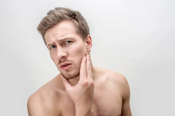 Ung man tittar rakt. Han trycker kinden med handen. Killen ser orolig. Isolerad på vit bakgrund. — Stockfoto