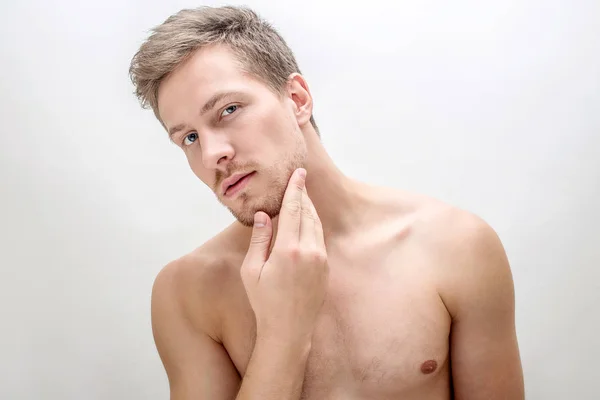 Un joven guapo que parece heterosexual. Toca la cara. El tipo no tiene camisa. Aislado sobre fondo blanco . — Foto de Stock