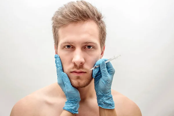 Allvarlig ung man se rakt. Kvinnan håller händerna på hans ansikte. Sprutan är riktad till läppar. Isolerad på vit bakgrund. — Stockfoto