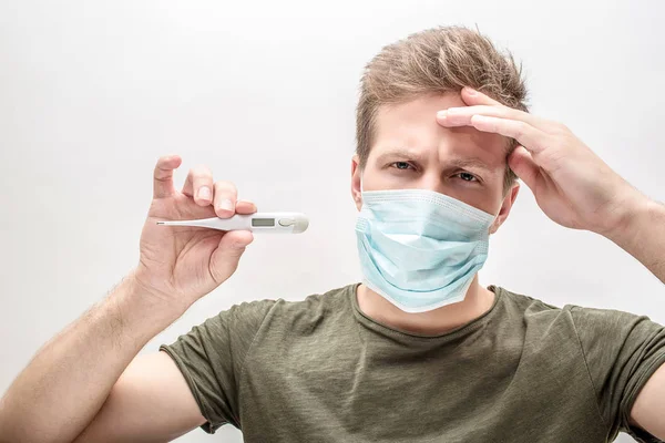 Un jeune homme malade tient le thermomètre à la main. Un autre est sur le front. Il a mal à la tête. Isolé sur fond blanc . — Photo